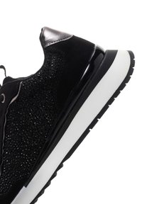 Sneaker nera con superficie in suede e tessuto testurizzato, un accento lucido nero e una suola bianca con un motivo di battistrada testurizzato.