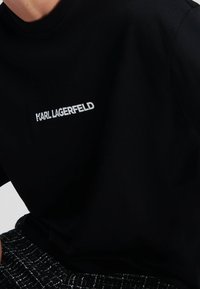 Svart kortärmad t-shirt i bomull med en vit broderad "KARL LAGERFELD" logotyp på bröstet. Slätt material.