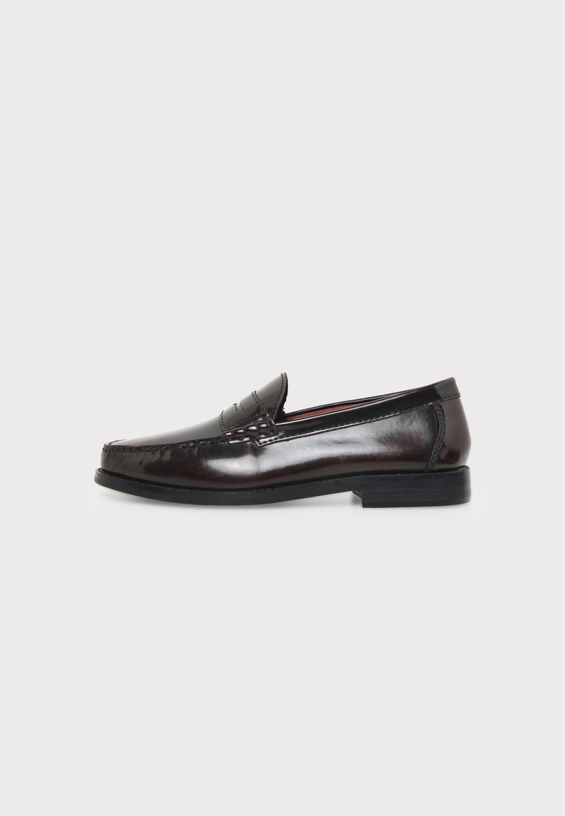 Mocassin penny en cuir marron foncé avec talon bas et détails cousus, présenté de profil sur un fond uni clair.