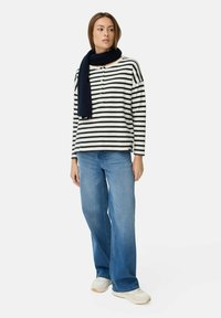 Gestreepte lange mouw top in marineblauw en crème, met een ronde halslijn, drie knopen, gecombineerd met lichtblauwe rechte jeans en witte sneakers.