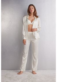 Zijden pyjama set in crèmekleur, met een button-down shirt en een elastische taillebroek, met daaronder een kanten bralette. Soepele textuur.