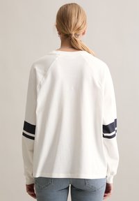 Weißes Langarmshirt mit marineblauen gestreiften Akzenten an den Ärmeln, aus weicher Baumwolle; verfügt über eine lockere Passform und einen runden Ausschnitt.