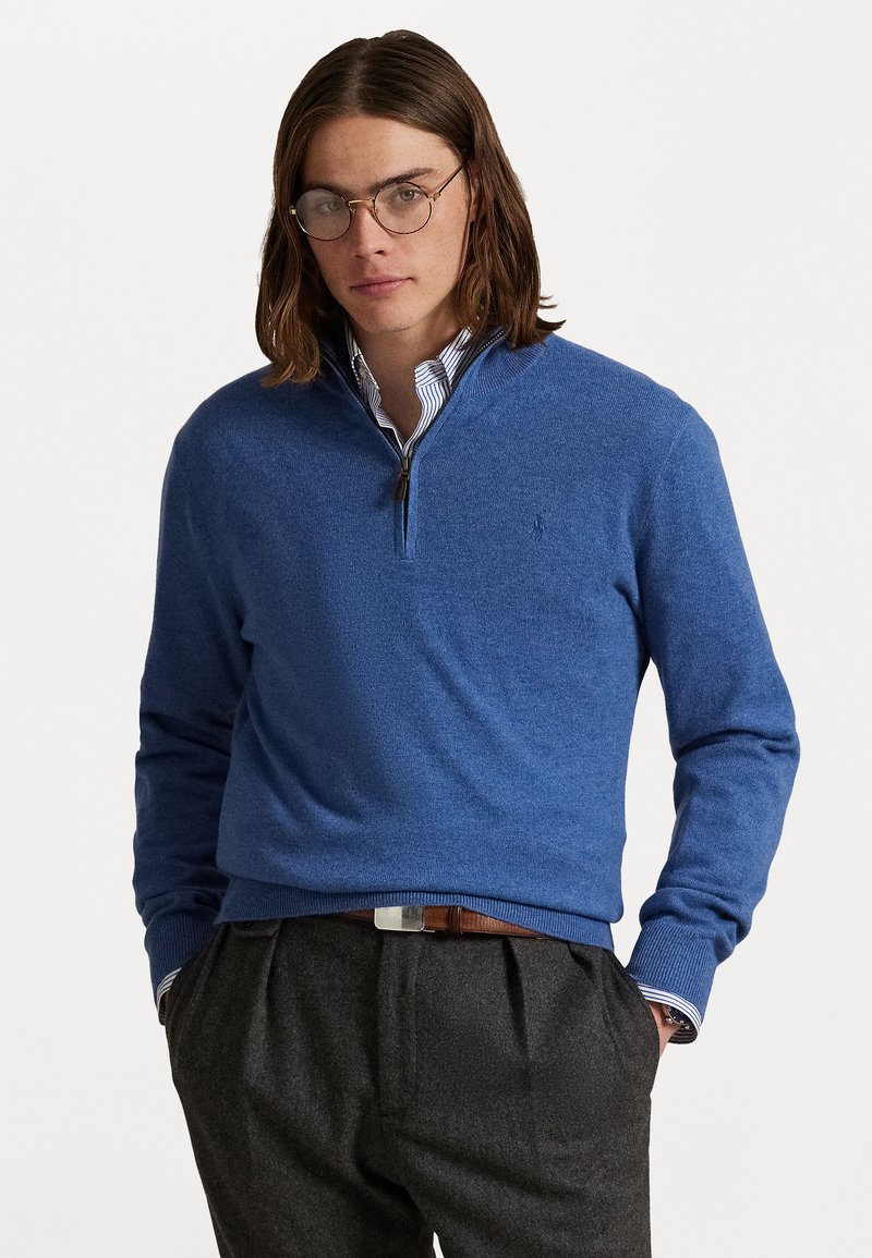 Blauwe zip-nekmuts gemaakt van gebreide stof, met een geribbelde zoom en manchetten. Draagt over een gestreept coll shirt, met donkere broek.