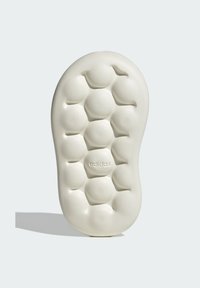 Suela de un zapato en color blanco roto, con un patrón texturizado de panal. Logo de "Adidas" en relieve cerca de la parte inferior. Acabado suave.