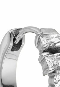 Silberring mit einem krallenartigen Design, das einen klaren, rechteckig geschliffenen Stein greift, der poliertes Metall und geometrische Textur präsentiert.