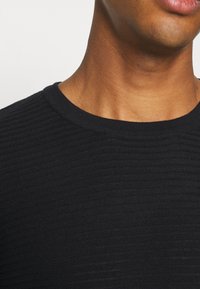 Czarny dzianinowy sweter z prążkowaną fakturą i okrągłym dekoltem. Tkanina wydaje się miękka i lekka, o gładkim wykończeniu.