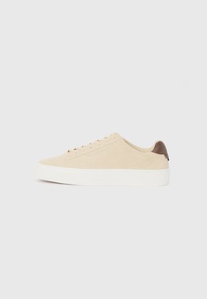 Beige suede sneaker with white rubber sole and light brown heel accent. Features flat laces and minimalist design for versatility.