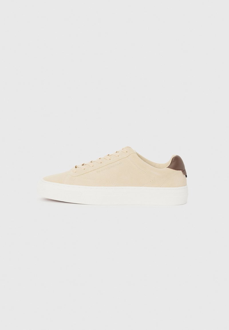 Beige suede sneaker with white rubber sole and light brown heel accent. Features flat laces and minimalist design for versatility.