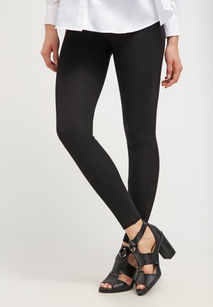 Leggings neri realizzati in un tessuto elasticizzato, abbinati a sandali neri con cinturini e tacco alto, caratterizzati da un tacco spesso e punta aperta.