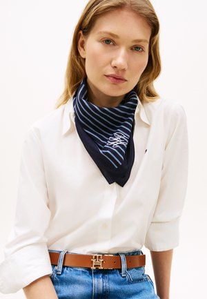 Tamsiai mėlynas šalikas su šviesiai mėlynomis juostelėmis ir baltu siuvinėtu logotipu, vilkimas su balta palaidine ir rudu diržu. Medvilnės medžiaga su minkšta tekstūra.