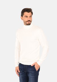 Maglione dolcevita bianco realizzato in un materiale morbido, con maniche lunghe e polsini a coste, abbinato a jeans in denim blu scuro.