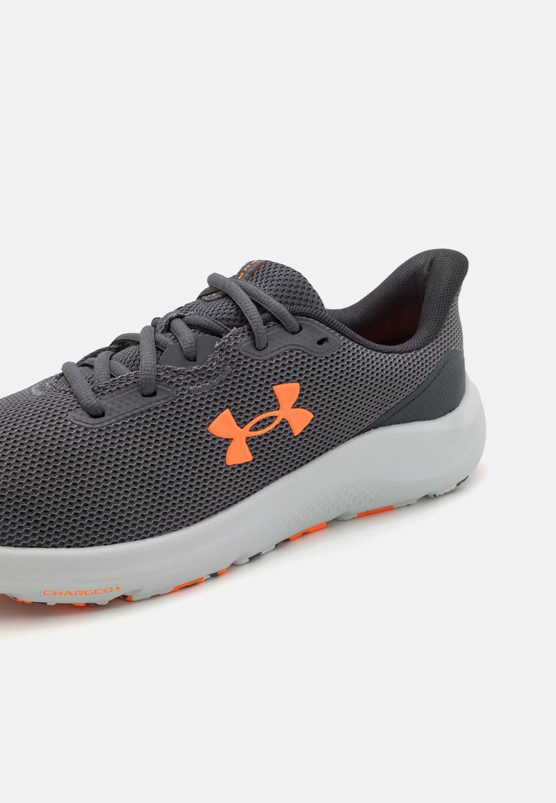 Chaussure de sport grise avec tige en maille, accents oranges, semelle rembourrée et orteil arrondi. Présente un logo bien visible sur le côté.