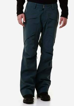 Pantaloni impermeabili di un verde scuro con vestibilità ampia, molteplici tasche e cerniere alle caviglie. Presentano una chiusura a bottone e un tessuto testurizzato.