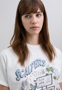 White short-sleeve t-shirt featuring a graphic print with the word "SCALPERS," playing cards, palm trees, and a sign with a skull and crossbones.