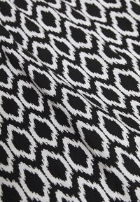 Černobílá vzorovaná tkanina s geometrickým vzorem obsahující prodloužené tvary, což vytváří texturovaný vzhled.