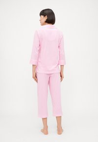 Rosa stripete pysjamasett med krageskjorte med trekvart ermer og cropped bukser, laget av myk stoff med en glatt tekstur.