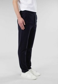 Marine joggesbukser med myk tekstur, elastisk midje, sidelommer og smal passform, parret med hvite sneakers.