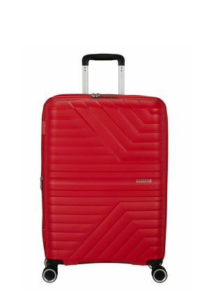 Valise rigide rouge avec des lignes diagonales texturées, quatre roues, poignée télescopique et logo American Tourister à l'avant.
