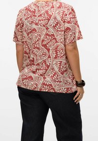 Camisa de manga corta en un color rojo óxido con un patrón floral y de paisley en crema. Corte holgado con un escote redondeado, hecha de una tela ligera.