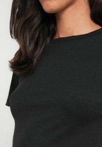 Μαύρο ριμπ τοπ με στρογγυλή λαιμόκοψη, κοντά μανίκια και απαλή υφή. Το ύφασμα φαίνεται ελαστικό και εφαρμοστό στο σώμα.