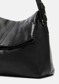 Zwarte leren schoudertas met een slouchy ontwerp, omslagflap en verstelbare schouderband. Glad textuur en subtiele logo-detail aan de zijkant.