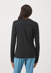 Černá dlouhá košile s hladkého, lehkého materiálu, s kulatým výstřihem a slim fit. Kombinace s volnými světle modrými kalhotami.