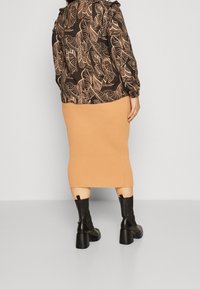 Svart och beige långärmad topp med lövmönster, ribbad beige midikjol och knähöga svarta klackstövlar. Mjukt tyg med texturer.