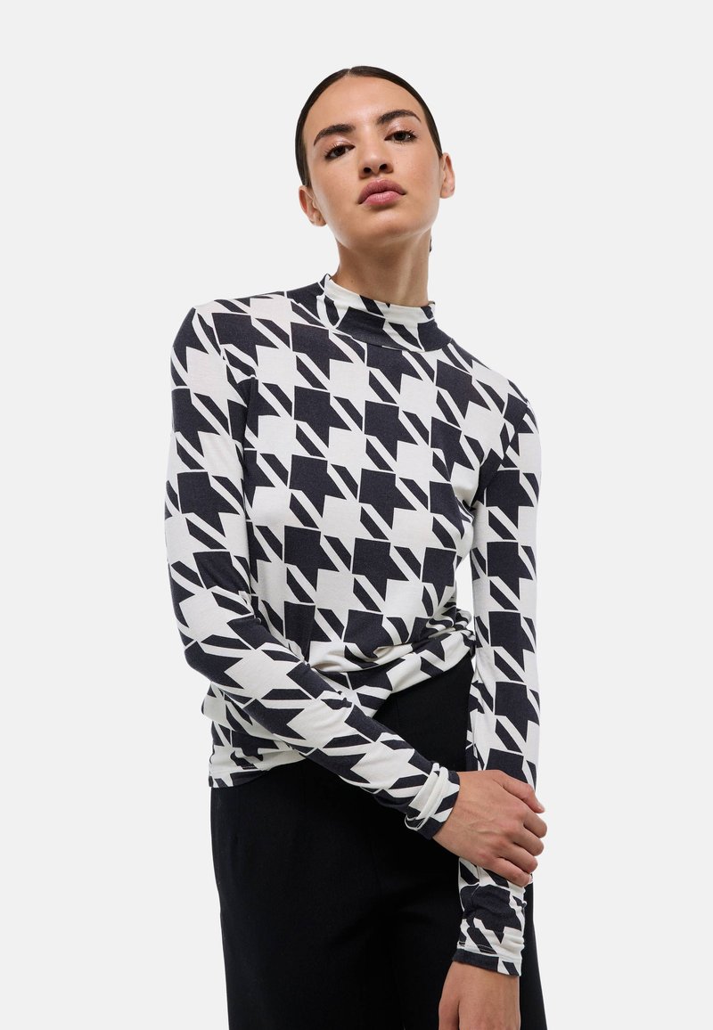 Haut à manches longues en tissu doux avec un motif géométrique noir et blanc. Col montant et design ajusté avec des manches slim.