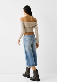 Beige ribbat off-the-shoulder topp, kort längd. Ljusblå vida denimculotter med urtvättad denim. Mörkbruna ankelstövlar med spännen.