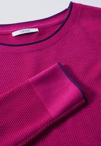 Maglione texturizzato magenta con collo rotondo e bordo blu navy, caratterizzato da un evidente motivo a nido d'ape e polsini a costine. Etichetta del marchio: CECIL.