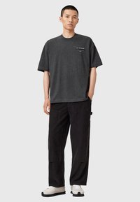 T-shirt en coton mélangé gris à manches courtes et coupe décontractée, associée à un pantalon en velours côtelé noir avec poches latérales et tissu texturé.