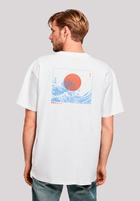 Witte katoenen t-shirt met een blauwe grafische ontwerp van golven en een rode zon op de achterkant, korte mouwen, relaxte pasvorm en ronde hals.