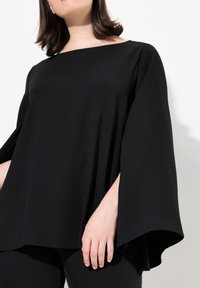 Top nero drappeggiato realizzato in tessuto morbido; presenta un ampio scollo e maniche larghe e fluide. Design semplice e minimalista con linee pulite.