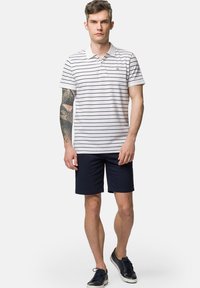 Biała polo z krótkim rękawem w granatowe paski, z kołnierzykiem, z małym logo, połączona z granatowymi szortami i casualowymi granatowymi sneakersami.