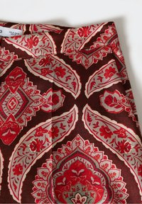 Tissu marron présentant des motifs paisley complexes rouges et crème avec des accents floraux. Texture lisse avec des formes et des couleurs définies.