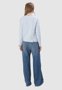 Hellblaues Langarmhemd mit rundem Ausschnitt, kombiniert mit locker sitzenden blauen Jeans. Verfügt über sichtbare Naht auf der Rückseite und ein kleines Logo-Detail.