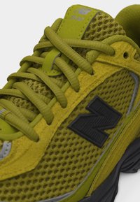 Geelgroene New Balance 509 sneaker met meshstof, suède overlays, zwart "N" logo, reflecterende details en dikke veters op een zwarte zool.