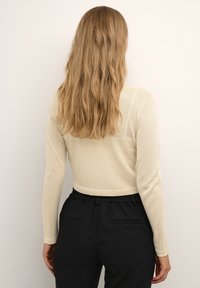 Beiges, langärmliges, geripptes Oberteil mit kurzem Schnitt und dezentem Schimmer. Kombiniert mit schwarzen Hosen mit elastischem Bund.