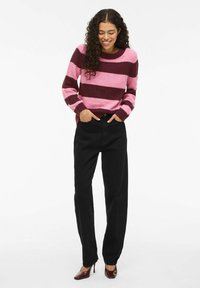 Strickpullover mit breiten rosa und burgunderfarbenen Streifen, rundem Halsausschnitt und gerippten Bündchen, kombiniert mit hoch taillierten schwarzen geraden Hosen und High Heels.