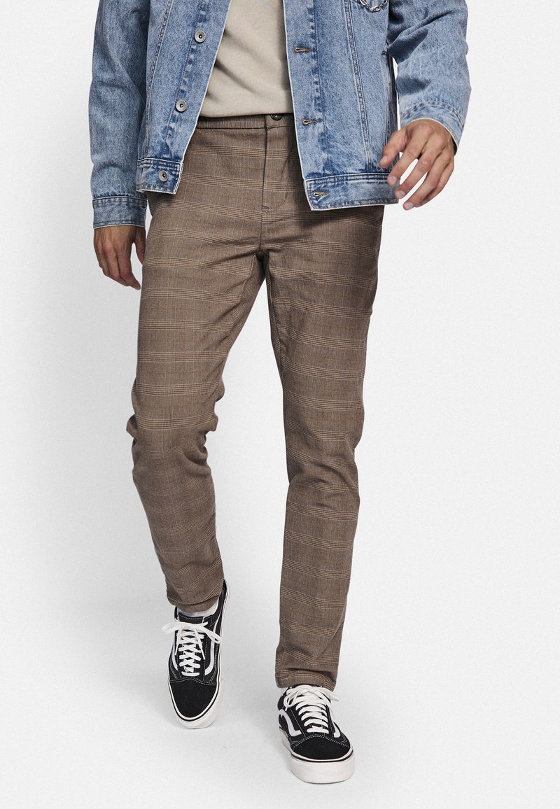 Bruna rutiga byxor med slim fit, gjorda av texturerat tyg. Bärs med en ljus denimjacka och svarta sneakers.