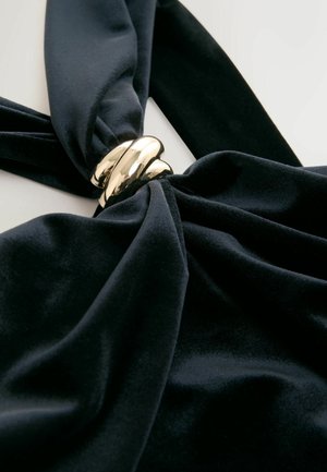 Czarna welwotowa tkanina skręcona w centrum, z błyszczącym złotym akcentem z metalowego skrętu. Gładka tekstura o bogatym, głębokim kolorze.