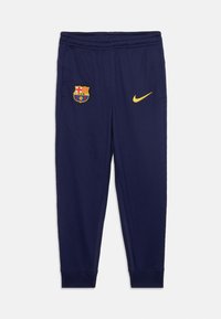 Mornarice plave atletske hlače s elastičnim pojasom, grb FC Barcelone na lijevom bedru i žuti Nike znak na desnom bedru.