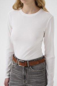 Kvinne iført en ensfarget hvit langermet skjorte stukket ned i høytlivete grå jeans med et brunt semsket belte med sølvspenne.