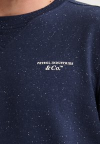 Navy-Sweatshirt aus strukturiertem Stoff mit hellen Sprenkeln. Es hat einen gerippten Ausschnitt und das Logo "Petrol Industries & Co." in Weiß.