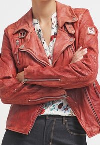 Red perforated leather motorcycle jacket with zip pockets, epaulets, and a double collar design, paired with a floral blouse underneath.