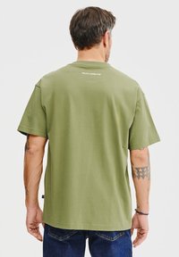 Zielona bawełniana koszulka z krótkim rękawem, prostym dołem i okrągłym dekoltem. Posiada małe białe logo na górnej części pleców.