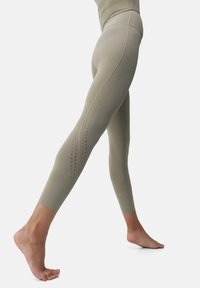 Hoge taille, licht olijfgroene legging gemaakt van rekbare stof, met een gladde textuur en geperforeerde accenten langs de zijkanten.