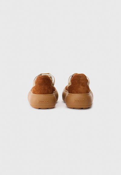 Prill pruunidest suede'ist ja nahast tossudest paksude kummitaldadega, millel on kanna peal embosseeritud "Moschino", vaadatuna tagant.