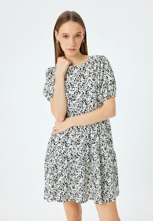 Musta-valkoinen pilkullinen mekko lyhyillä puffihihnoilla, pyöreällä kaula-aukolla ja levenevällä hameella. Kevyt kangas, jossa on pehmeä texture.