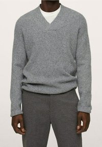 Grauer Strickpullover mit V-Ausschnitt, geripptem Muster und langen Ärmeln, kombiniert mit grauen Hosen, die eine lockere Passform und weichen Stoff aufweisen.